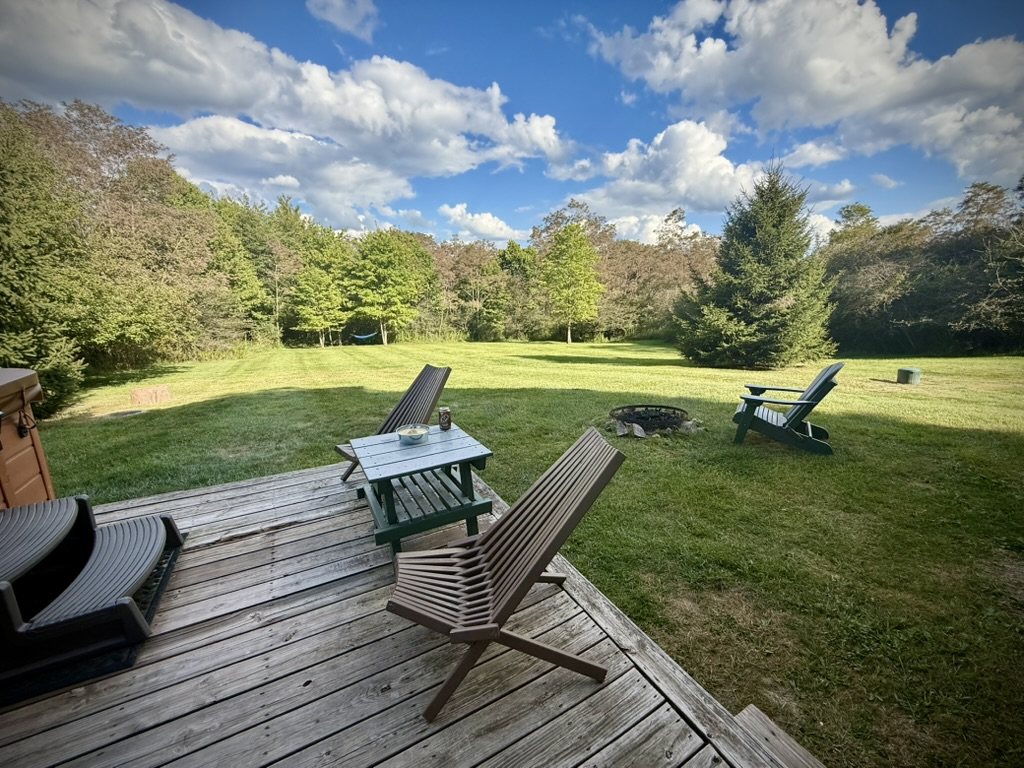 Back deck chairs looking over the wide lawn, fire pit and tree line