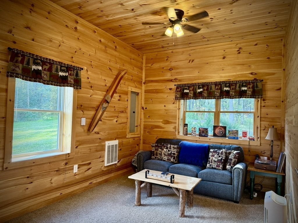 Knotty-pine sitting room with a blue sofa, rustic coffee table and windows onto the woods